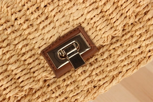 Detail shot of beige woven crossbody bag with gold metal clasp and brown leather patch