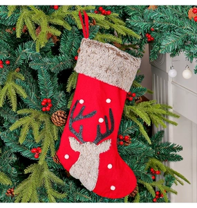 Detail of red plush Christmas stocking with reindeer faux fur and white pom-poms on tree