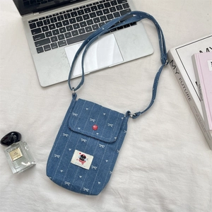 Detail van blauwe denim crossbodytas met sterrenpatroon, rode knoop en cartoon patch