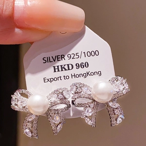 Detail of 925 silver bow earrings with round white pearls and pavé cubic zirconia