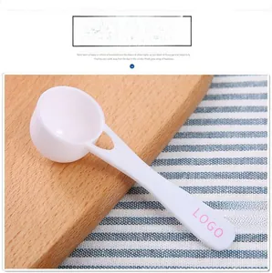 Close-up of white plastic measuring spoon on wood board showing custom logo handle detail