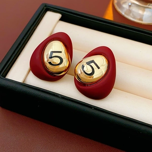 Detail of burgundy oval earrings featuring a gold metallic center with number 5 engraving