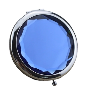 Portable round silver metal makeup mirror with a faceted blue gemstone on the lid