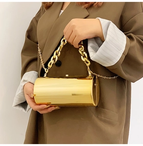 Detail of gold mirror cylindrical clutch with chunky handle and metallic chain strap
