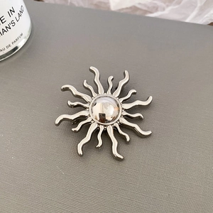 Detailed view of sunburst silver metal brooch on a textured grey background surface