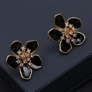 Macro detail of black enamel flower earrings with golden edges and tiny crystals