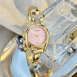 Detail of pink dial and gold horseshoe watch case on metallic and glass tray