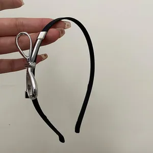 Detail of a slim black headband featuring a sleek silver metallic bow accent held by hand