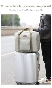 Light gray large capacity travel bag with front pocket sitting on a silver suitcase handle