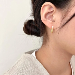 Close-up of elegant gold U-shaped earrings with white pearls worn by a model