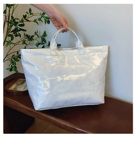 Close-up of a white glossy waterproof tote bag with embossed lettering on a wooden bench