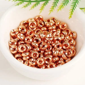 Close-up of numerous rose gold 18K plated wheel spacer beads in a white bowl for DIY jewelry