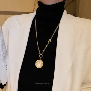 Détail du collier doré avec lettre B et pendentif en nacre sur pull noir