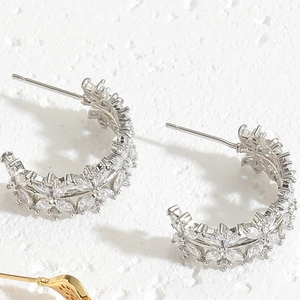 Detailed macro view of silver C-shaped earrings with leaves and sparkling zircon stones