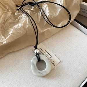 Close-up of a minimalist necklace with marble ring, silver bead and black cord detail