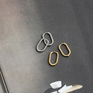 Detail shot of silver and gold beaded U-shaped hoop earrings on textured surface