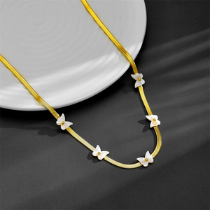 Detail of gold snake chain necklace featuring white shell butterfly charms on a white plate
