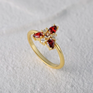 Macro detail of gold flower ring featuring three pear-cut red stones and diamond accents