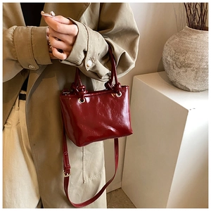 Détail du sac seau bordeaux en cuir verni brillant avec poignée nouée et bandoulière amovible