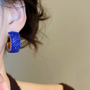 Macro shot of blue crystal-encrusted C-shaped earrings with gold metal base for women