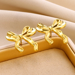 Detailed close-up of golden bow-shaped earrings with unique fluid metal texture and gloss