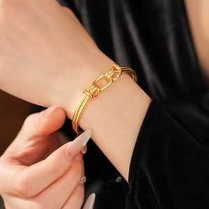 Detail shot of a gold-plated knot bangle bracelet worn on a wrist against black velvet
