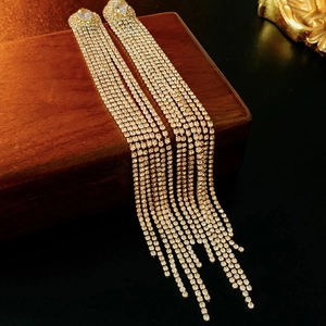 Gros plan de boucles d'oreilles à longs pompons dorés et strass sur fond de bois sombre