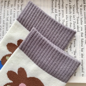Close-up of gray ribbed cuffs and white knitted socks with floral patterns on a book