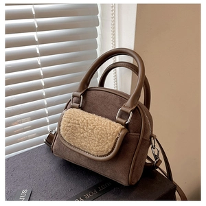 Detail of dark brown suede handbag featuring beige faux shearling trim and round handles