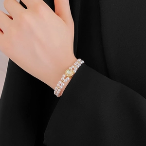 Macro detail of double-layer pearl bracelet with gold flower and moonstone on wrist