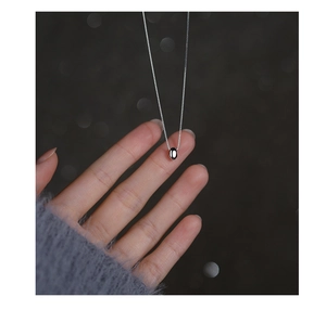 Macro shot of minimalist silver bean pendant on fine chain held by fingers