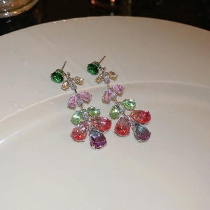 Detailed macro view of colorful teardrop zircon earrings on a white porcelain tray