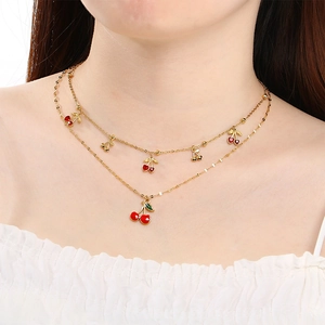Detail of a double-layered gold cherry necklace with red cherry pendants on a model