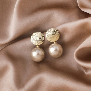 Detailed view of elegant gold-textured metal earrings with large champagne imitation pearls