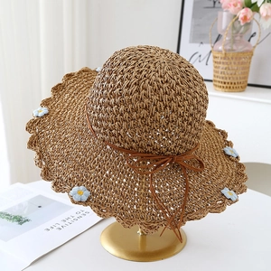 Close-up of woven straw sun hat featuring daisy embroidery and wavy brim details