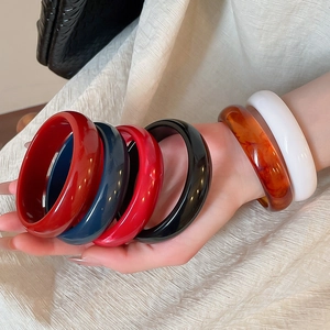 Close-up of stacked colorful resin bangles in amber, red, and blue on a model's wrist