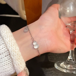 Detail of silver chain bracelet with white gourd pendant and diamond heart on wrist