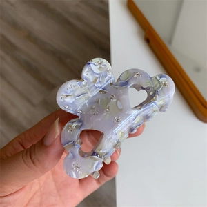 Close-up of acetic acid hair claw with marble texture, rhinestones and heart cutout