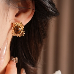 Close-up of golden irregular mesh earring with brown oval tiger eye stone on model
