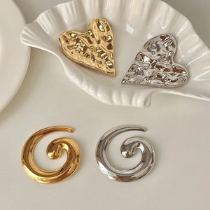 Elegant gold and silver stainless steel heart and spiral brooches on white shell tray