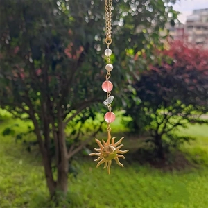 Golden sun pendant charm featuring colorful crystal beads on a delicate chain outdoors