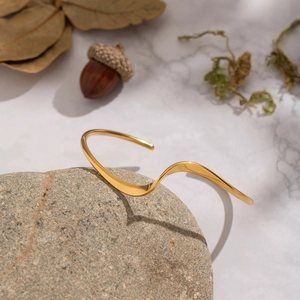 Detail of a wavy 18K gold-plated open bracelet placed on a natural rock with dry leaves