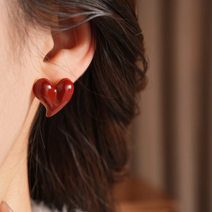 Close-up of a model wearing minimalist red heart stud earrings with a glossy gold finish