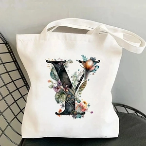 Detail of white canvas tote bag featuring floral letter Y print on a modern mesh chair