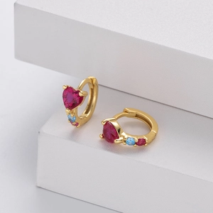 Detailed view of gold huggie earrings with heart ruby and blue diamond accents