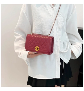 Detail of burgundy quilted leather crossbody bag with golden clasp worn by a model