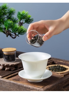 Close-up of loose tea leaves being poured into a white ceramic cup from a glass jar