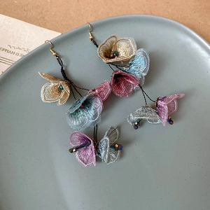 Detail of floral tassel earrings featuring blue fabric petals and gold butterfly motifs