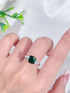 Close-up of emerald-cut green gemstone ring with side baguette stones on a hand