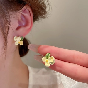 Detail view of flower stud earrings featuring soft yellow petals and green leaves